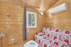 A wooden cabin room with a bed, a window, a wall-mounted air conditioner, and a heart-shaped decoration. - Cottage "Morgon" with Mountain View, Wi-Fi and Air Conditioning (Crots)