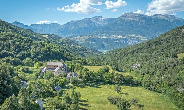 A mountainous landscape with a building surrounded by lush greenery and a valley. - Cottage “Morgon” with Mountain View, Wi-Fi, and Air Conditioning (Crots)