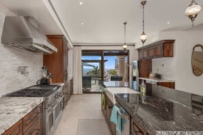 A modern kitchen with a large island, stainless steel appliances, and a view to the outdoors.