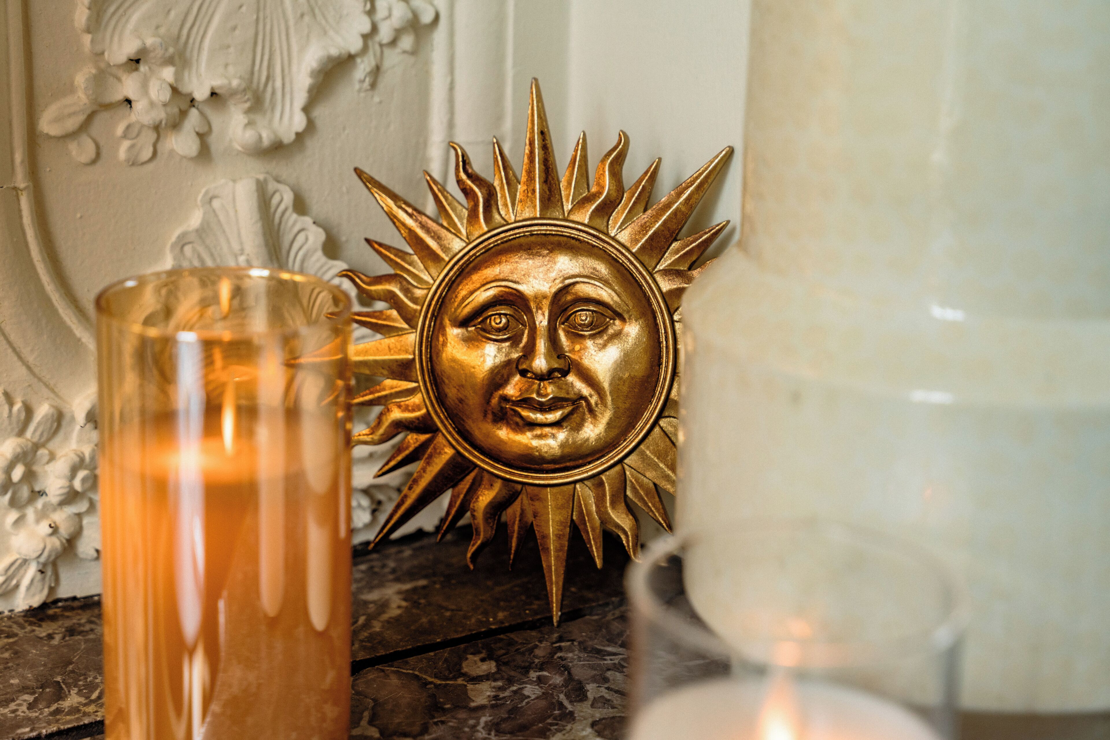 A decorative sun with a face, a candle, and a vase.