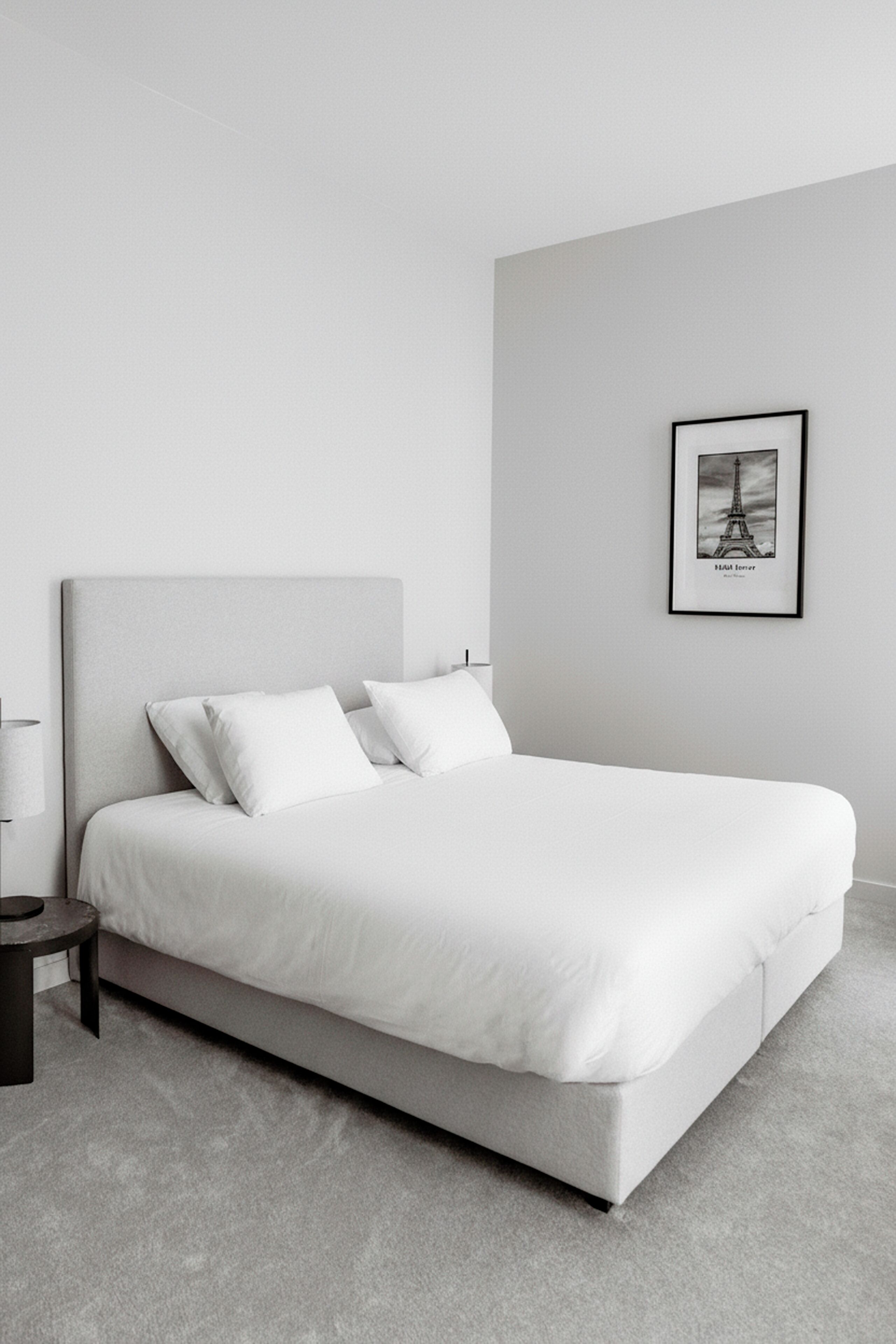 A minimalist bedroom with a large bed, a small bedside table, and a framed picture on the wall.