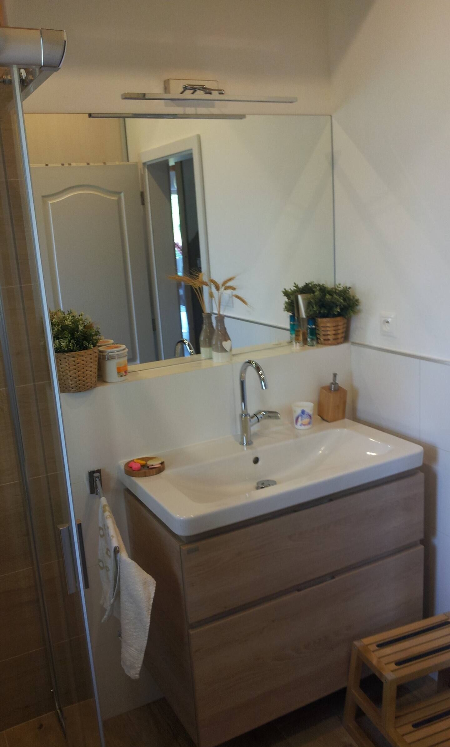 Une salle de bain avec un lavabo blanc, un miroir et un tabouret en bois.