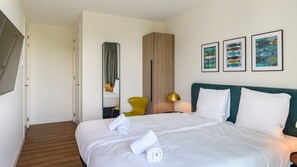 Una habitació d'hotel amb un llit, una cadira, un mirall i obres d'art a la paret.