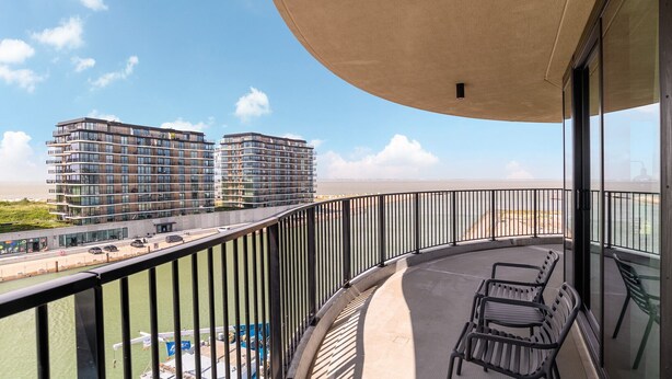Un balcon offrant une vue sur deux immeubles de grande hauteur, une étendue d’eau et une côte lointaine.
