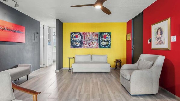 Una sala de estar moderna con un sofá, dos sillones, un ventilador de techo y obras de arte en las paredes.