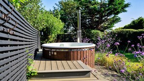 A hot tub with a wooden deck and a metal pole in a garden setting. - Firethorn (Bude)