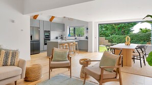A modern kitchen with grey cabinets, a central island, and a dining area with wooden chairs and a table. - Firethorn (Bude)