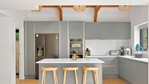 A modern kitchen with grey cabinets, a white island with stools, wooden flooring, and a hanging light fixture. - Firethorn (Bude)