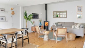 A modern living room with a wooden dining table, chairs, a sofa, and a large plant. - Firethorn (Bude)
