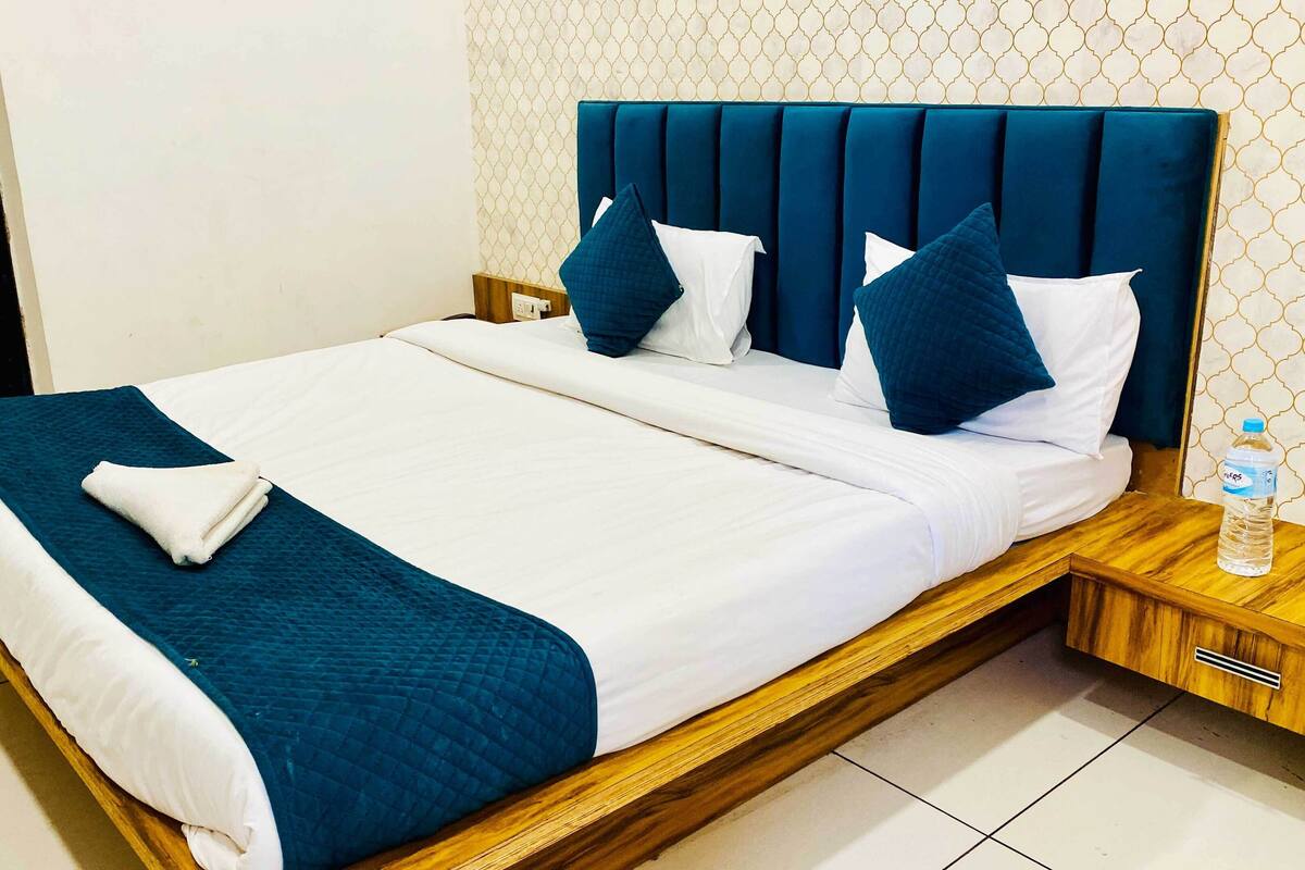 A neatly made bed with a blue headboard, white bedding, and a folded towel.