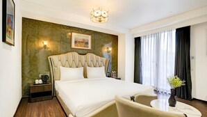A modern hotel room with a large bed, a small table, a chair, and a view of the outdoors through the window.
