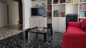 Un salon doté d’un sol en marbre noir, d’un canapé rouge, d’une table basse en verre, d’un téléviseur à écran plat et d’une bibliothèque remplie de livres et d’objets décoratifs.