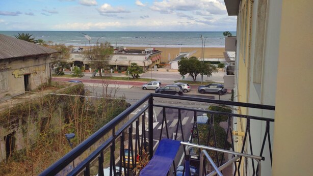 Un balcon donnant sur une plage, une route avec des voitures et des bâtiments en arrière-plan.