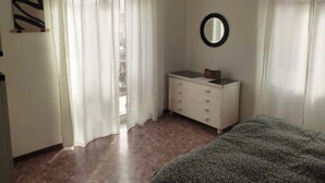 Une chambre à coucher avec un lit, une commode, un miroir et une fenêtre avec des rideaux.