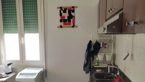 Une cuisine équipée d’une cuisinière à gaz, de meubles blancs, d’une fenêtre avec des stores et d’un tapis bleu.