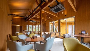 Un interior moderno con vigas de madera, mesas redondas y sillas de colores claros.