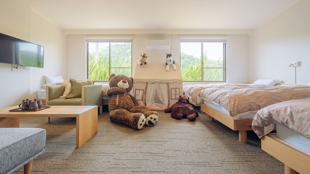Une chambre avec deux lits, un canapé, une table et une structure en forme de tente, décorée avec des peluches.