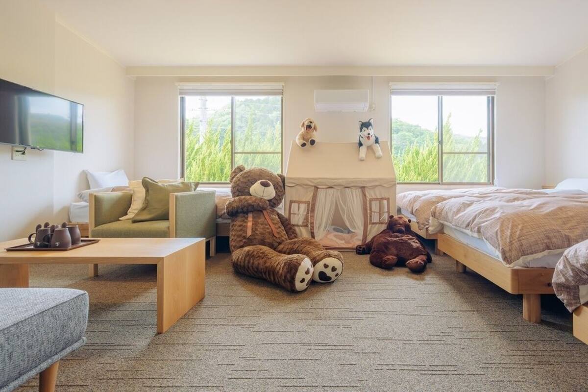 Une chambre avec deux lits, un canapé, une table et une structure en forme de tente, décorée avec des peluches.