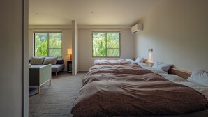 Un dormitorio con una cama grande, dos ventanas, una mesita de noche, una lámpara y una zona de estar con un sofá y una pequeña mesa.