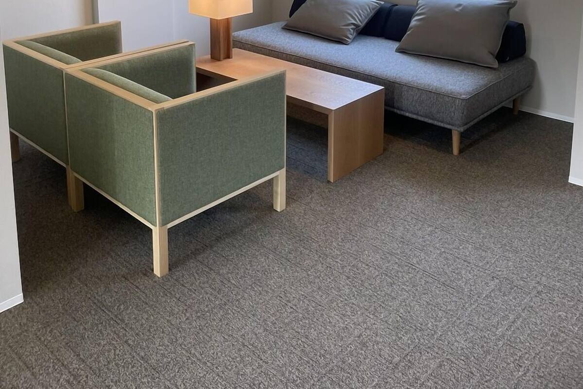 Un salon moderne comprenant un canapé, deux fauteuils, une table basse, un téléviseur et une fenêtre avec des stores.