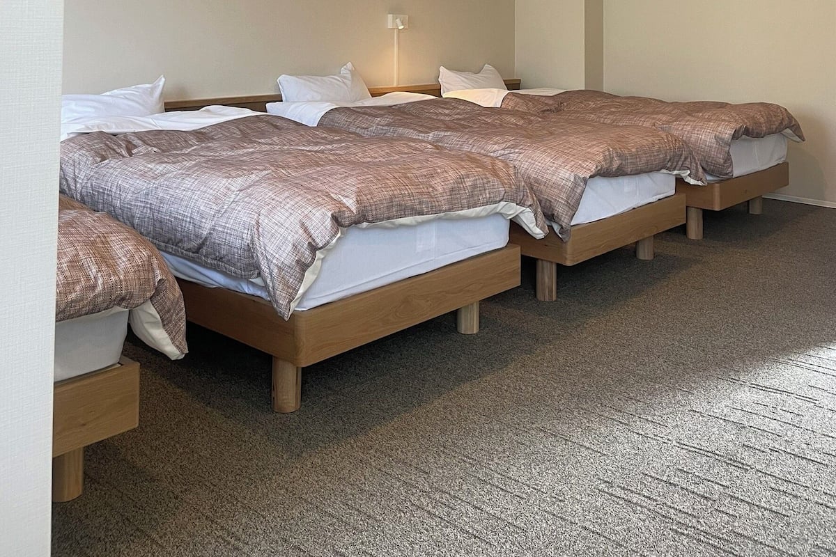 Een hotelkamer met vier eenpersoonsbedden, een nachtkastje, een wandlamp en een vloerbedekking.