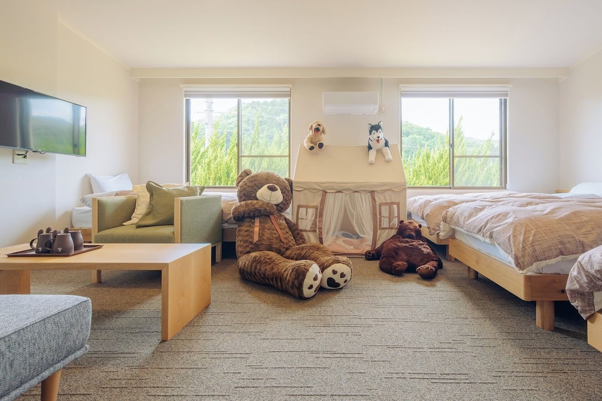 Slaapkamer met een bed, een bank, een klein tafeltje, een teddybeer, een speeltent en een televisie.