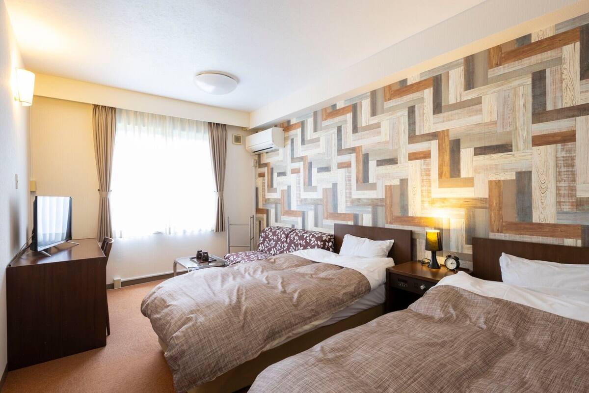 Een hotelkamer met twee bedden, een televisie, een bureau, een lamp en een muur met een geometrisch patroon.