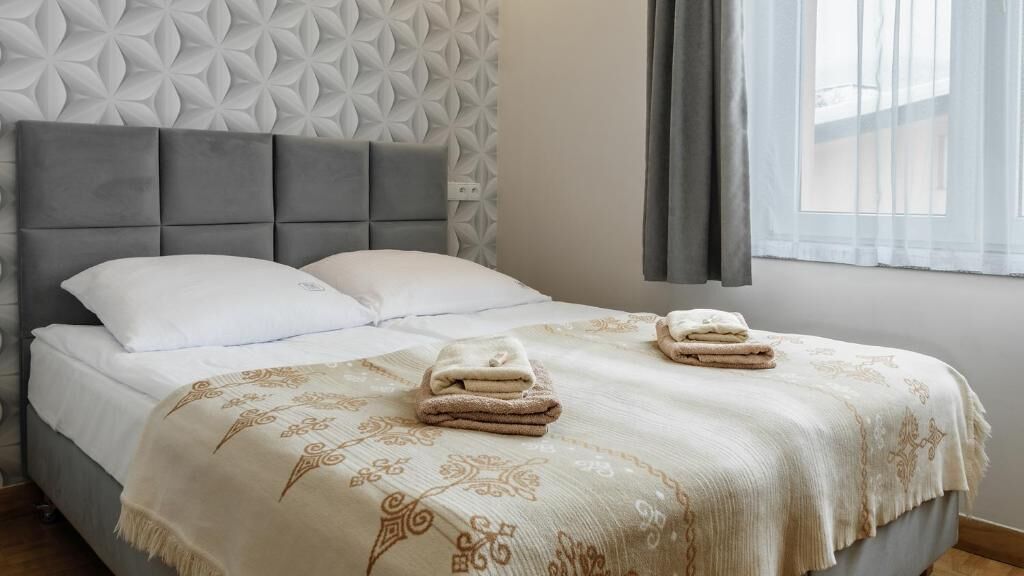 A neatly made bed with a patterned bedspread and two folded towels.