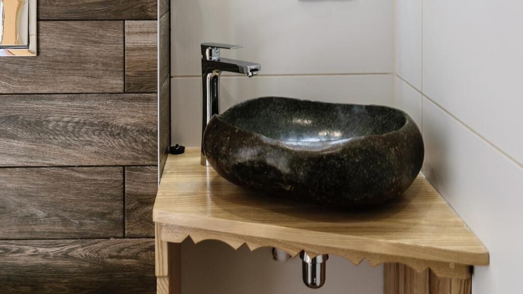 A modern bathroom with a wooden vanity, a stone sink, and a chrome faucet.