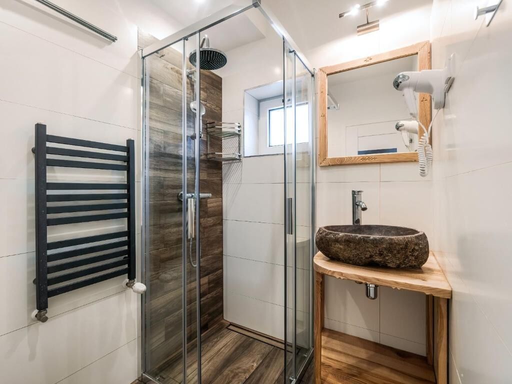 A modern bathroom with a glass shower enclosure, a wooden vanity with a stone basin, and a towel rack.
