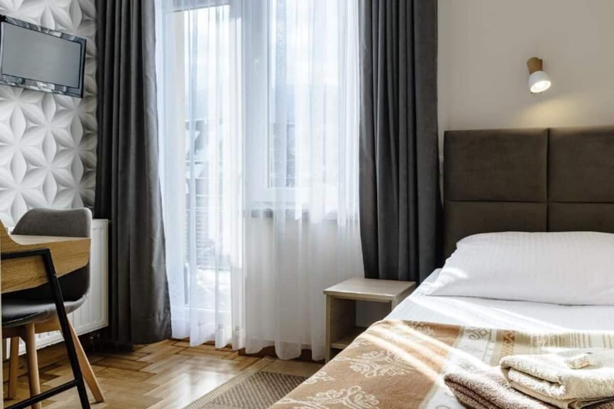 A hotel room with a bed, a desk, a TV, and a window with curtains.
