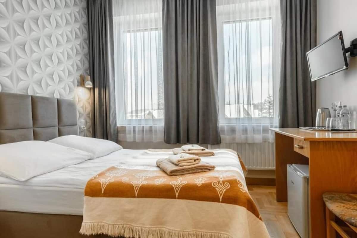 A hotel room with a bed, a desk, a TV, and a view of the outside through large windows.