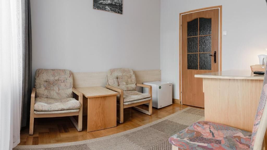 A compact room with two chairs, a small table, a refrigerator, and a wooden door with a glass panel.