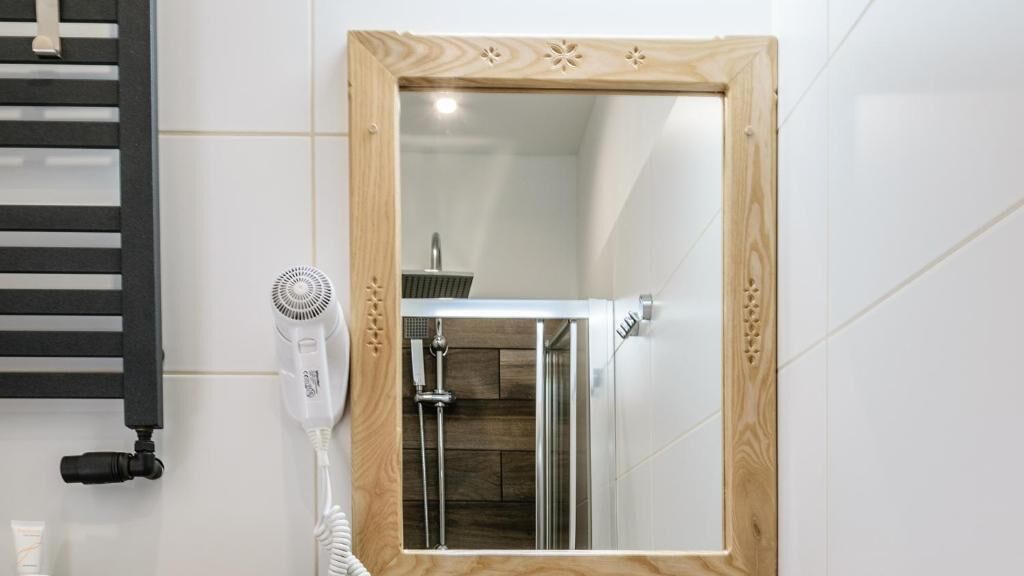 Een badkamer met een spiegel met houten lijst, een witte muur en een zwarte handdoekhouder.