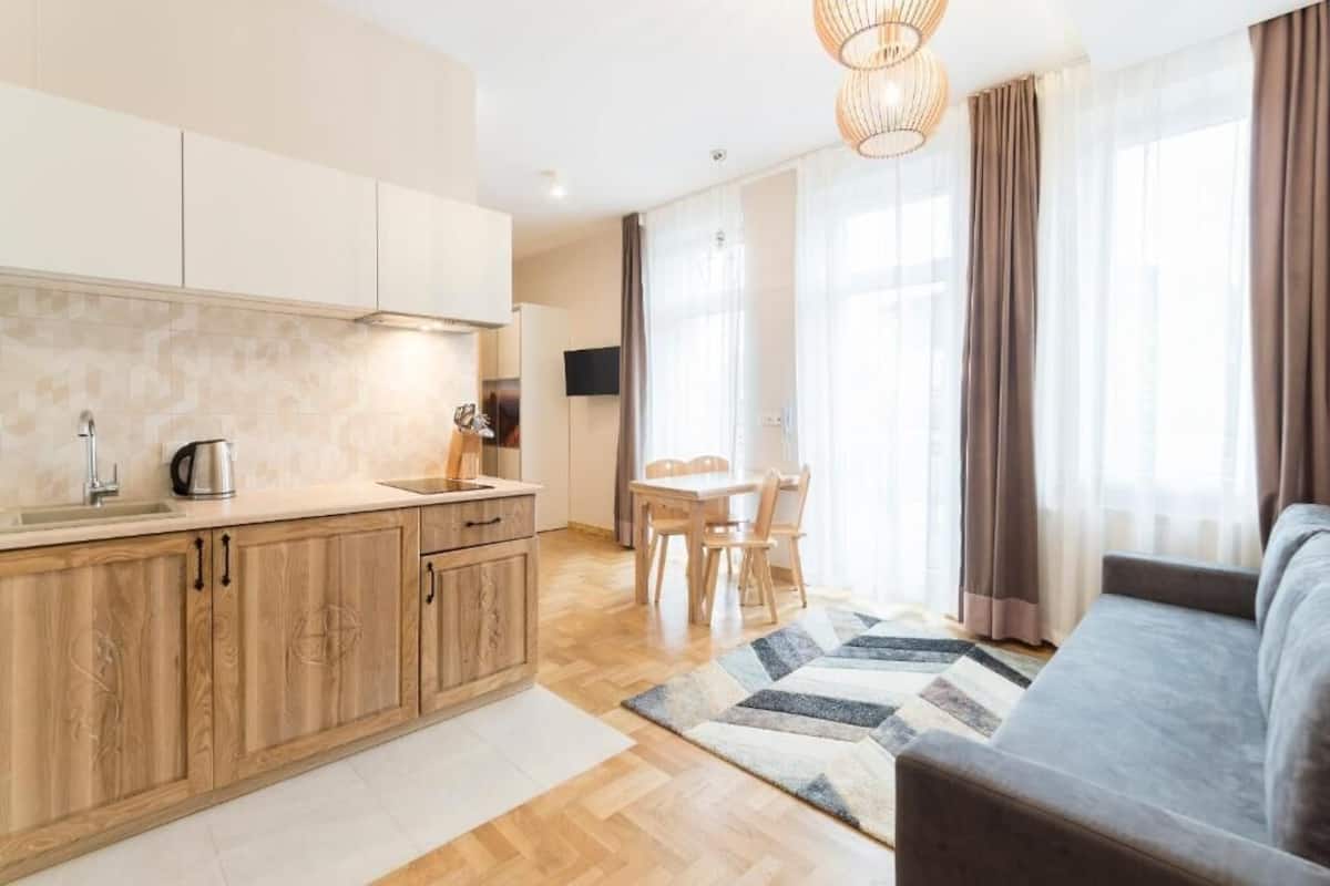 A modern kitchen with wooden cabinets, a dining area with a table and chairs, and a living area with a sofa and a rug.