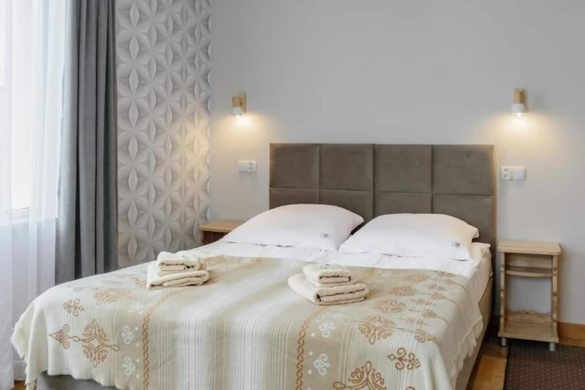 A neatly made bed with a patterned bedspread and pillows, two bedside lamps, and a small wooden nightstand.