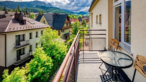 A balcony with a table and chairs, overlooking a village and mountains. - AMI ZAKOPANE (Zakopane)