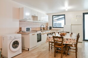 Una cucina compatta con lavatrice, forno a microonde e forno. C'è un tavolo da pranzo con sedie e una finestra con vista.