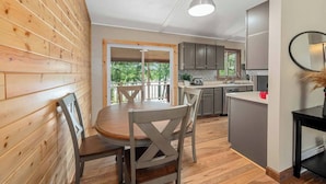 Un intérieur de chalet chaleureux comprenant un coin repas, une cuisine et un balcon offrant une vue sur les arbres.