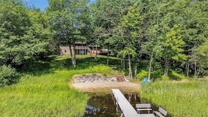 Un chalet rustique avec un quai s’avançant dans un étang, le tout entouré d’une végétation luxuriante.