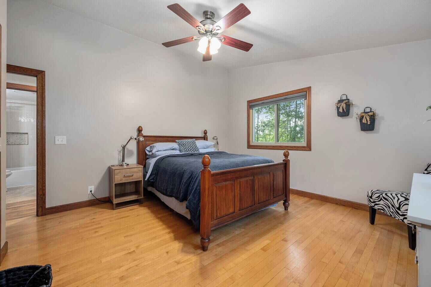 A bedroom with a wooden bed, a nightstand, a ceiling fan, a window, and a view of the outdoors.