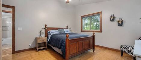 A bedroom with a wooden bed, a nightstand, a ceiling fan, a window, and a view of the outdoors.