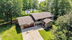 Une maison à deux étages avec un garage, entourée d’arbres et offrant une vue sur un lac.