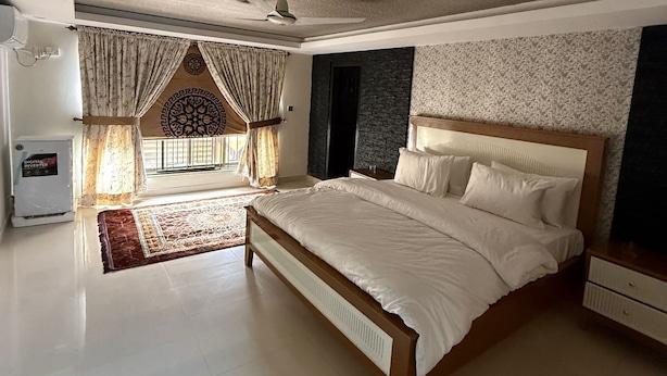 A spacious bedroom with a large bed, a ceiling fan, and a view of the outside. - Sundas Lodge (Islamabad)