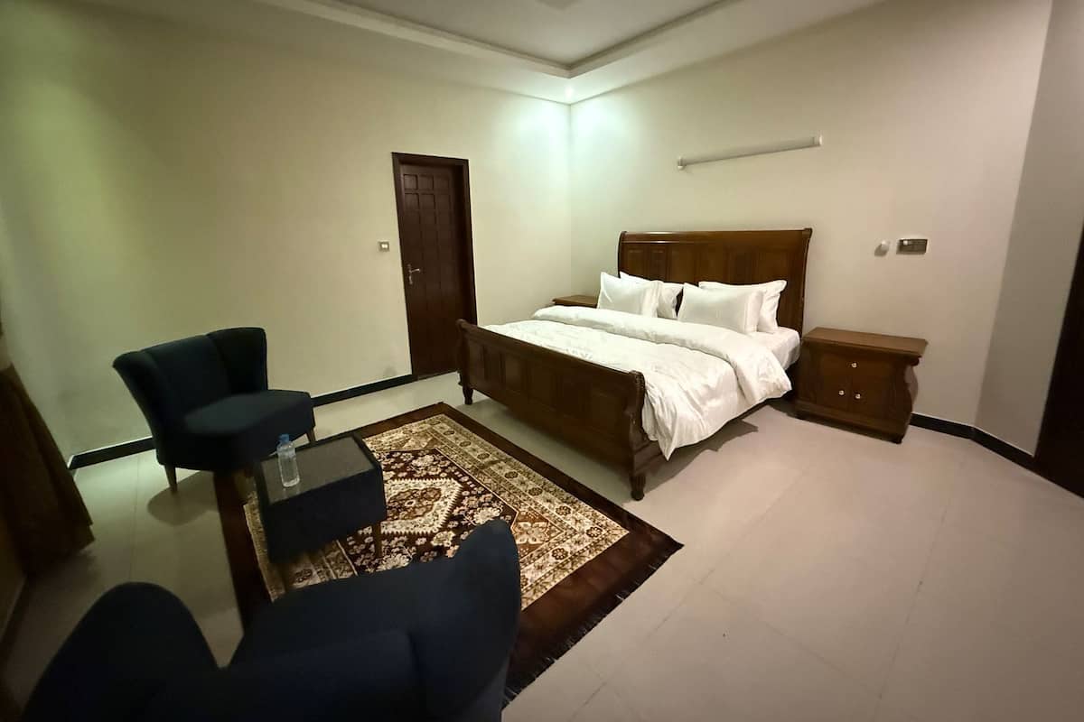 A bedroom with a bed, a chair, a nightstand, a door, and a ceiling fan.