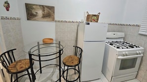 Une cuisine compacte équipée d’un réfrigérateur, d’une cuisinière et de deux chaises disposées autour d’une petite table.