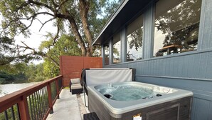 Un jacuzzi con un banco de madera y una zona de estar cubierta, rodeado por una terraza con barandilla.