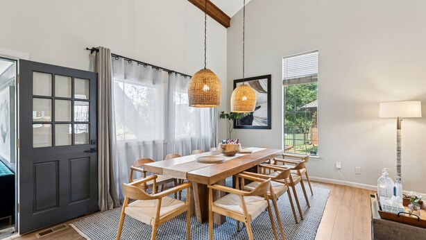 Un comedor con una mesa y sillas de madera, una lámpara colgante y vista al exterior a través de una ventana.