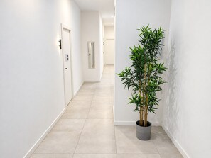 A hallway with a potted plant, white walls, and a tiled floor.