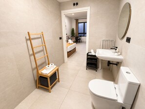 A modern bathroom with a toilet, sink, and mirror. There is a wooden ladder with towels on it, and a small cart with toiletries.